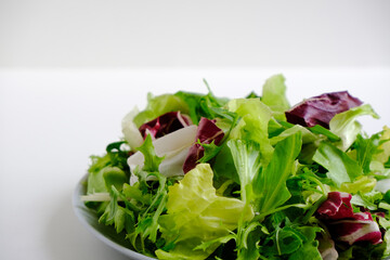 Bright fresh juicy raw salad greens. Escalora salad, frisee, radicchio, arugula salad in a gray plate on a white plate. Diet healthy food. Low-calorie, nutritious meal. Health care. Vitamin bowl. 