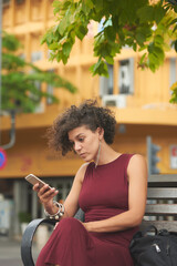 Fototapeta na wymiar Portrait of serious young elegant woman with curly hair reading article or text message on her phone