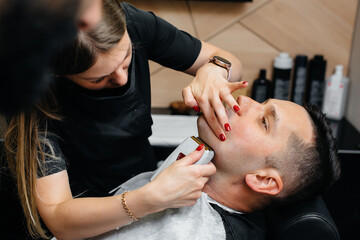 Obraz na płótnie Canvas A professional stylist in a modern stylish barbershop shaves and cuts a young man's hair. Beauty salon, hair salon