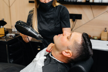 A professional stylist in a modern stylish barbershop shaves and cuts a young man's hair. Beauty salon, hair salon