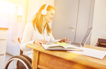 Behinderte junge Frau im Rollstuhl am Computer bei Fernstudium