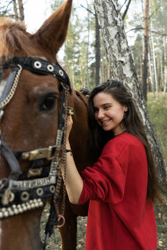 A beautiful long-haired girl in a red hoodie stands near the horse.