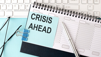 CRISIS AHEAD text on blue sticker on planning and keyboard,blue background