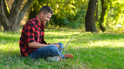 Young man using laptop, freelancer working online outdoors, typing on keyboard, chatting on computer.