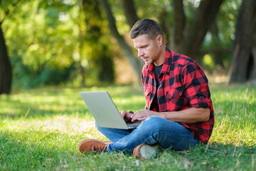 Man using laptop, freelancer working online outdoors, typing on keyboard, chatting on computer.