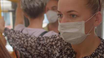 Using a face mask while traveling on public transport. Young woman holding a handrail in a city tram, close-up portrait.