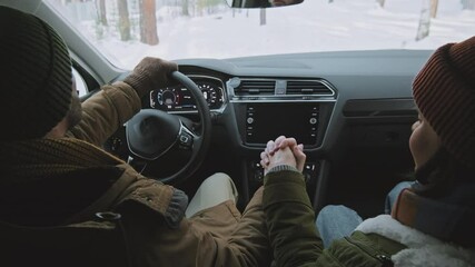 Handheld shot from inside of moving car man holding his girlfriends hand while driving along narrow road covered in snow