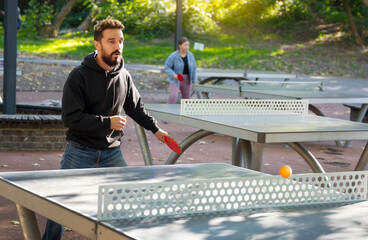 Street table tennis on the open air ground. Game focused man plays ping pong.