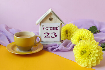 Calendar for October 23 : decorative house with the name of the month in English with the numbers 23, a bouquet of yellow dahlias on a light pastel scarf, side view, multi-colored background