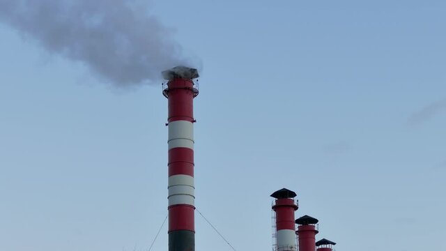 Chimney smoke / Smoke stack / Air pollution. Smoke comes from red-white chimneys on thermoelectric plant against sky...Unmodified camera color.