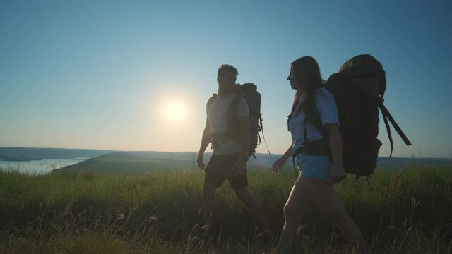 The man and woman with backpacks trekking along the river coast. slow motion