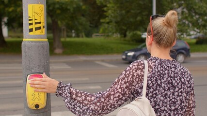Female pedestrian presses a traffic light button to cross the road. The innovative contactless push...