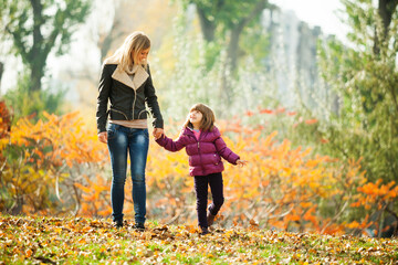 Mother and daughter walking in park in autumn.