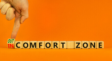 Out or in comfort zone symbol. Businessman turns a wooden cube and changes words 'in comfort zone' to 'out comfort zone'. Beautiful orange background, copy space. Business, psychology concept.