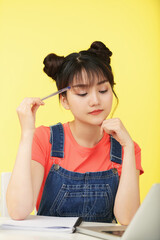Portrait of pensive young Asian teenage girl doing homework and pointing at temple with pen and doing doing difficult task © DragonImages