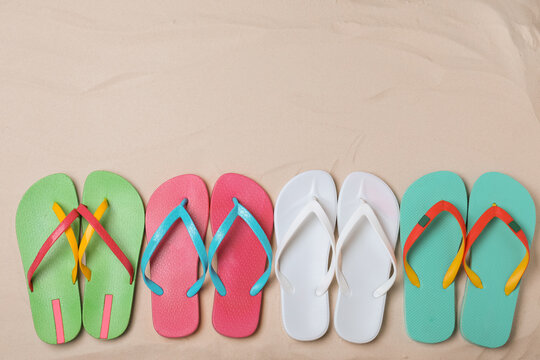 Different bright flip flops on sand, flat lay. Space for text