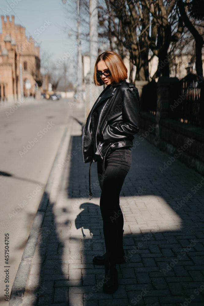 Canvas Prints young girl in a black leather jacket stands on the background of a city street.