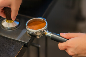 Man is using a tamper to press freshly ground morning coffee into a coffee tablet