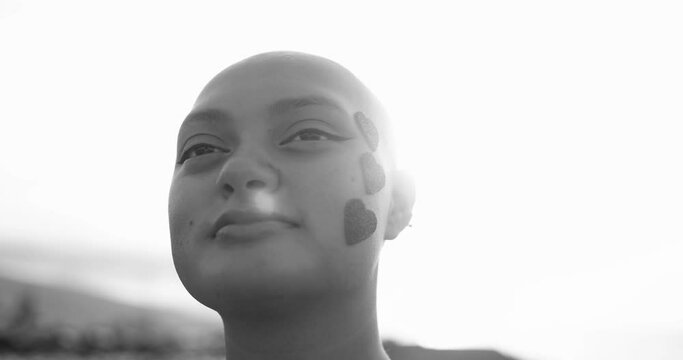 Young bald girl with heart stickers on her face posing in front of camera at sunset - Black and white video