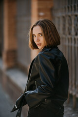 Fototapeta premium Young woman in sunglasses, hat and black leather jacket posing outdoor.