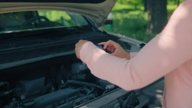 Female taking photo under the car hood, sending to auto repair center, help