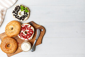 Sweet bagels with butter cream and fresh berries. On a wooden board. Overhead, horizontal, with space