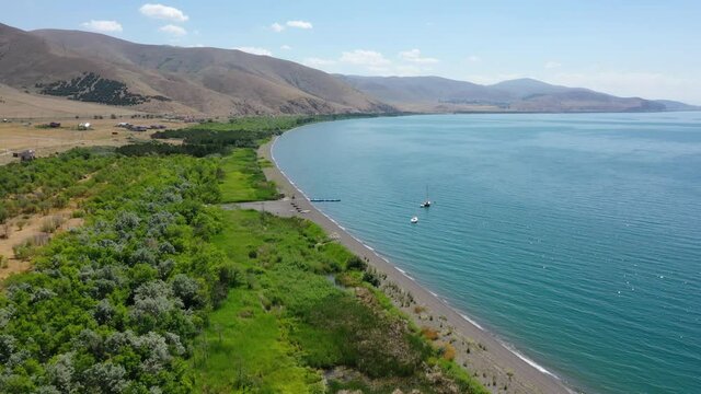 Famous Lake Sevan with clear water in Armenia, aerial view. Drone camera's show forest near lake,  boat in water, in background mountains. Discovery Armenia. Touristic place.
