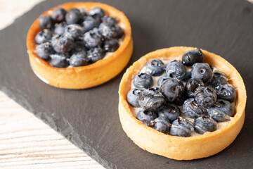 Fresh blueberry tarts on a black plate. Homemade bilberry tartlets. Fruit dessert with blueberries