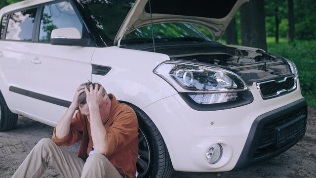 Annoyed male sitting near the faulty automobile on the roadside, car repair