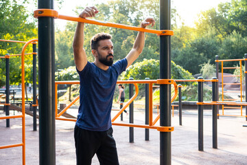 Fototapeta premium Open air sport ground, street training. Charismatic athletic man trains on the horizontal bar at the street.