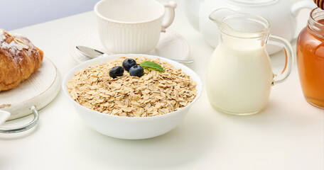 Raw oatmeal in white ceramic plate on white table, breakfast, close up