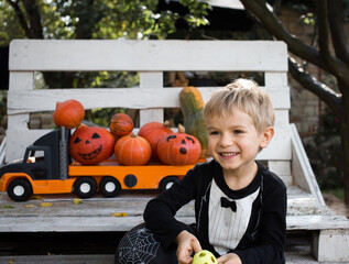 Fototapeta premium focus is on the merry boy 4-5 years old at the Halloween party. In the background is a large children's toy car, loaded with dozens of orange pumpkins