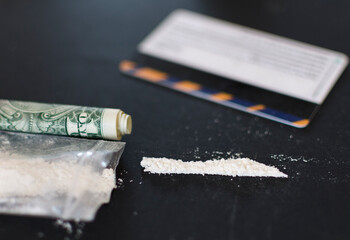 Money and cocaine. Addiction. Drug's use. Hundred dollar bills, white powder (like cocaine) on the close of the black table. Illegal drugs and dirty money. Lots of cocaine.
