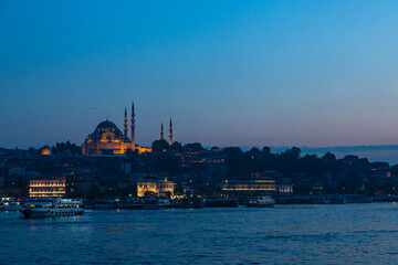 Fototapeta premium トルコ イスタンブールの夕暮れ時の金角湾と旧市街の街並みと丘の上に建つライトアップされたスレイマニエ・モスク