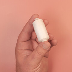 A spool of white thread in a man's hand. Square format