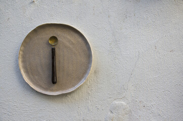 Abstract conceptual photo of empty ceramic glazed plate, dish, bowl with hand made spoon isolated on white rough wall in unknown patio in old Town in Lithuania 