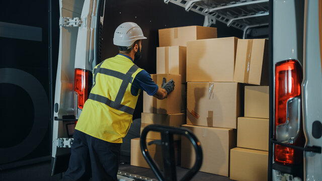 Handsome Latin Male Worker Wearing Hard Hat Loads Cardboard Boxes into Delivery Truck. Delivering Online Orders, E-Commerce Goods, Food, Medicine Supply. Overworked Tired Frontline Hero Doing Job