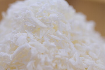 Coconut shavings in a wooden bowl against a white background. Food.