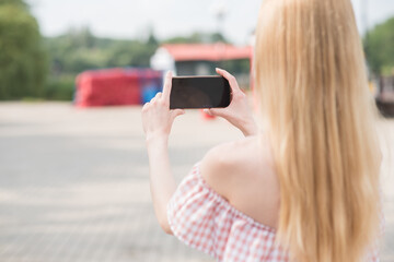 Beautiful caucasian blonde girl holding a smartphone in her hands and taking picture