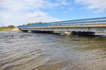 A concrete bridge for cars across a forest river on a sunny spring day in northern Russia.