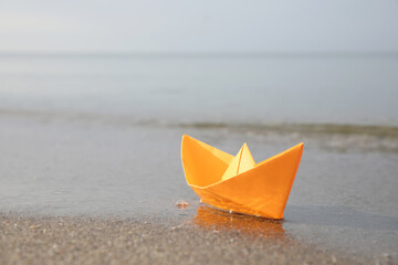 Fototapeta na wymiar Orange paper boat on sandy beach near sea, space for text