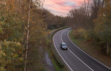 Fototapeta premium Autumn landscape. Country road with a car going through the forest