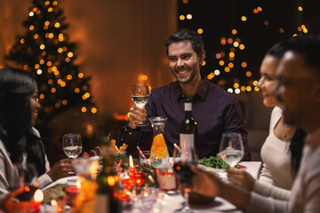 holidays, party and celebration concept - multiethnic group of happy friends having christmas dinner at home and drinking wine