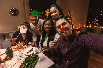 holidays, friendship and celebration concept - multiethnic group of happy friends with party props having christmas dinner at home and taking selfie © Syda Productions