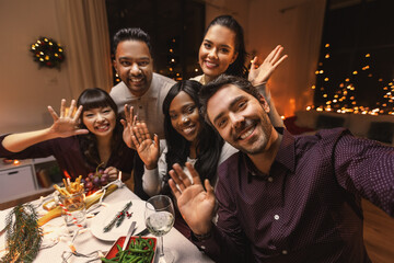 holidays, friendship and celebration concept - multiethnic group of happy friends having christmas dinner at home and taking selfie