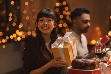 holidays, party and celebration concept - happy smiling woman holding gift box on christmas dinner...