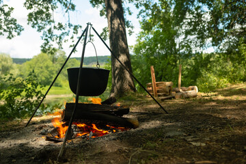 Tourists prepare lunch in hiking pot on campfire at campsite. Bowler on bonfire. Soup boils in cauldron.