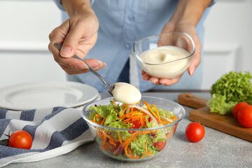 Woman adding mayonnaise to delicious salad at grey table, closeup - obrazy, fototapety, plakaty