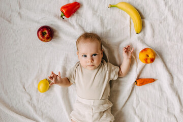 three months old baby lying among different fruits and vegetables. Food diversification concept.
