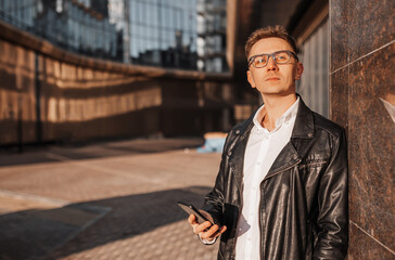 Handsome man with glasses with a smartphone on the street of a big city. Businessman talking on the phone on urban background